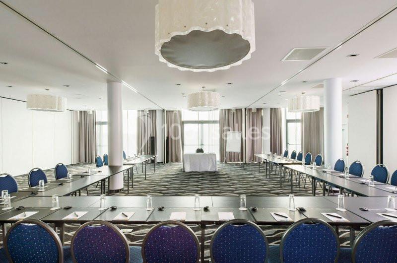 Location salle Mons (Hainaut) - Congrès Hôtel Mons Van Der Valk #8 Salle de réunion lumineuse avec des tables disposées en U, des chaises bleues et un tableau de présentation.