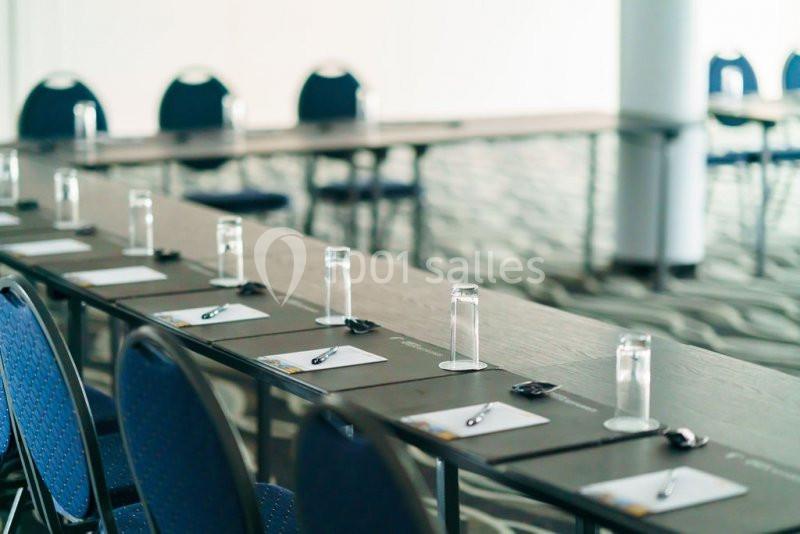 Location salle Mons (Hainaut) - Congrès Hôtel Mons Van Der Valk #12 Salle de réunion avec des tables alignées, des verres, des stylos et des blocs-notes disposés devant des chaises bleues.