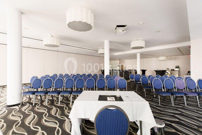 Location salle Mons (Hainaut) - Congrès Hôtel Mons Van Der Valk #13 Salle de conférence lumineuse avec rangées de chaises bleues, table à l'avant et décor sobre.