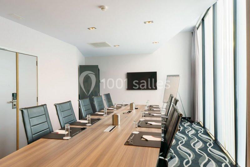 Location salle Mons (Hainaut) - Congrès Hôtel Mons Van Der Valk #14 Salle de réunion moderne avec une grande table en bois, des chaises noires, un écran mural et un tableau blanc.