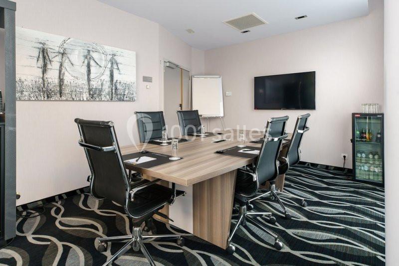 Location salle Mons (Hainaut) - Congrès Hôtel Mons Van Der Valk #15 Salle de réunion moderne avec table rectangulaire, chaises noires, écran mural, tableau blanc et minibar.