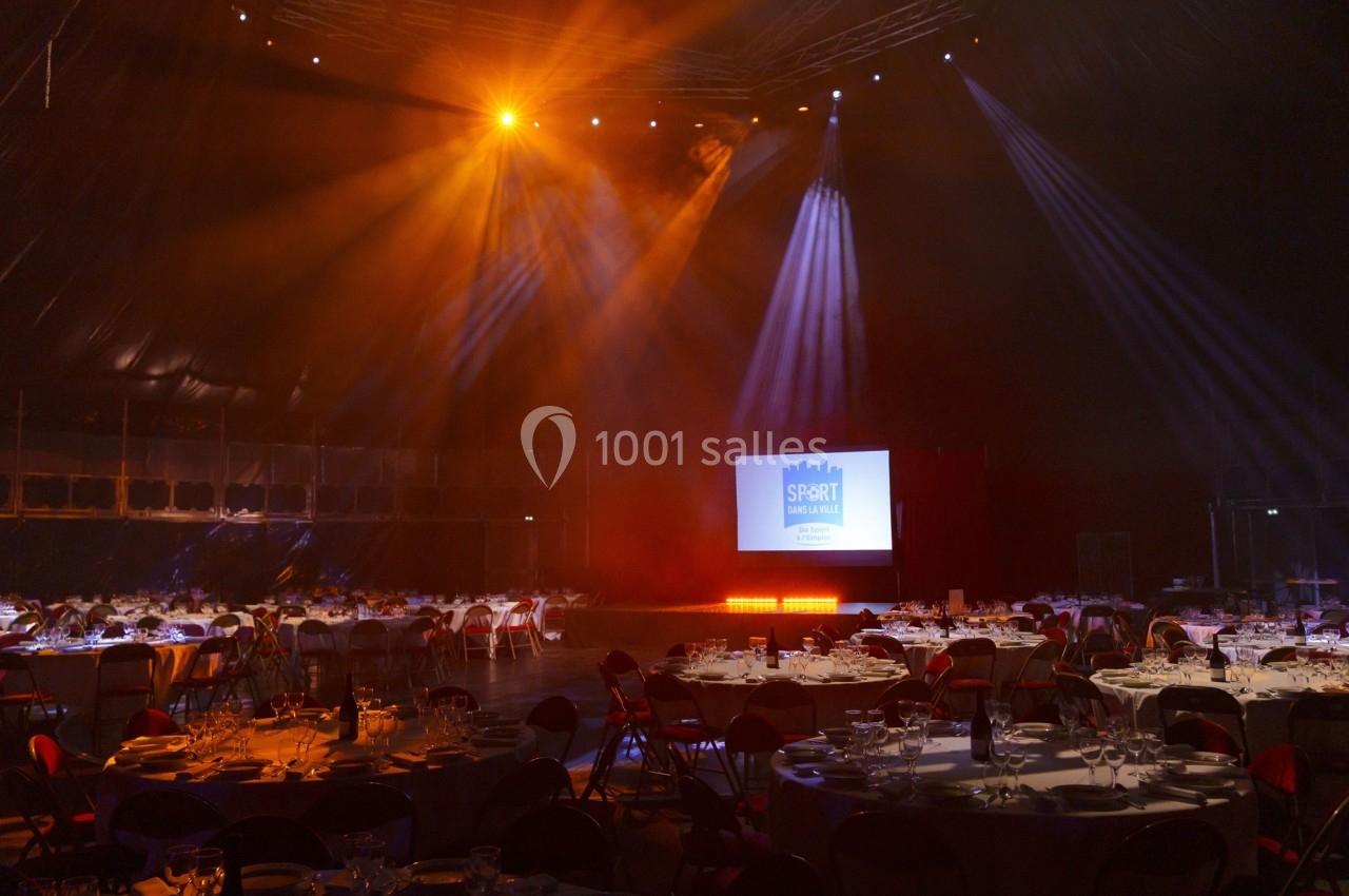 Salle de réception éclairée avec des tables dressées et un écran de projection affichant un logo.