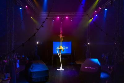 Un acrobate réalise une figure sur un tissu aérien sous un chapiteau éclairé par des lumières colorées.