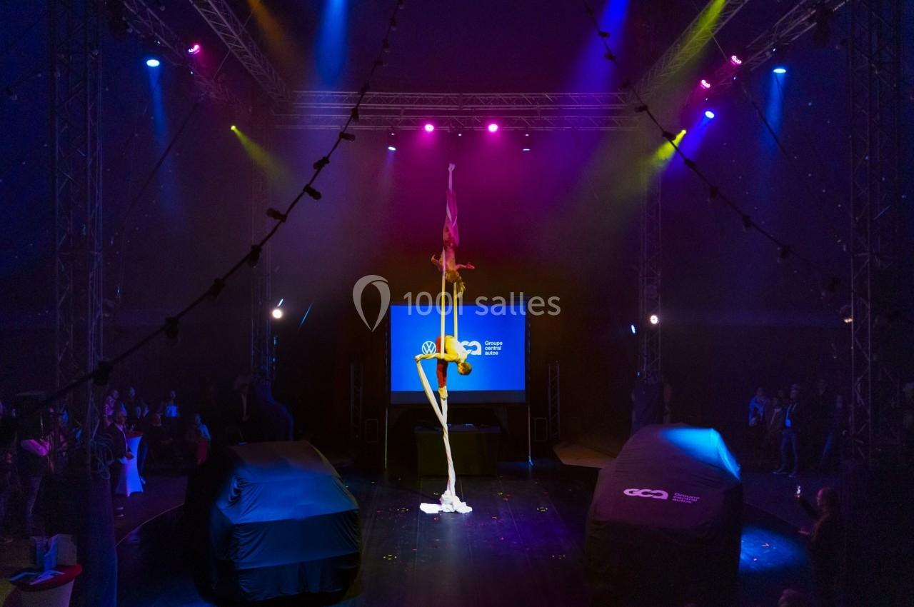 Un acrobate réalise une figure sur un tissu aérien sous un chapiteau éclairé par des lumières colorées.