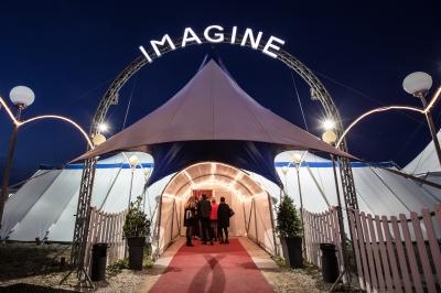 Un acrobate réalise une figure sur un tissu aérien sous un chapiteau éclairé par des lumières colorées.