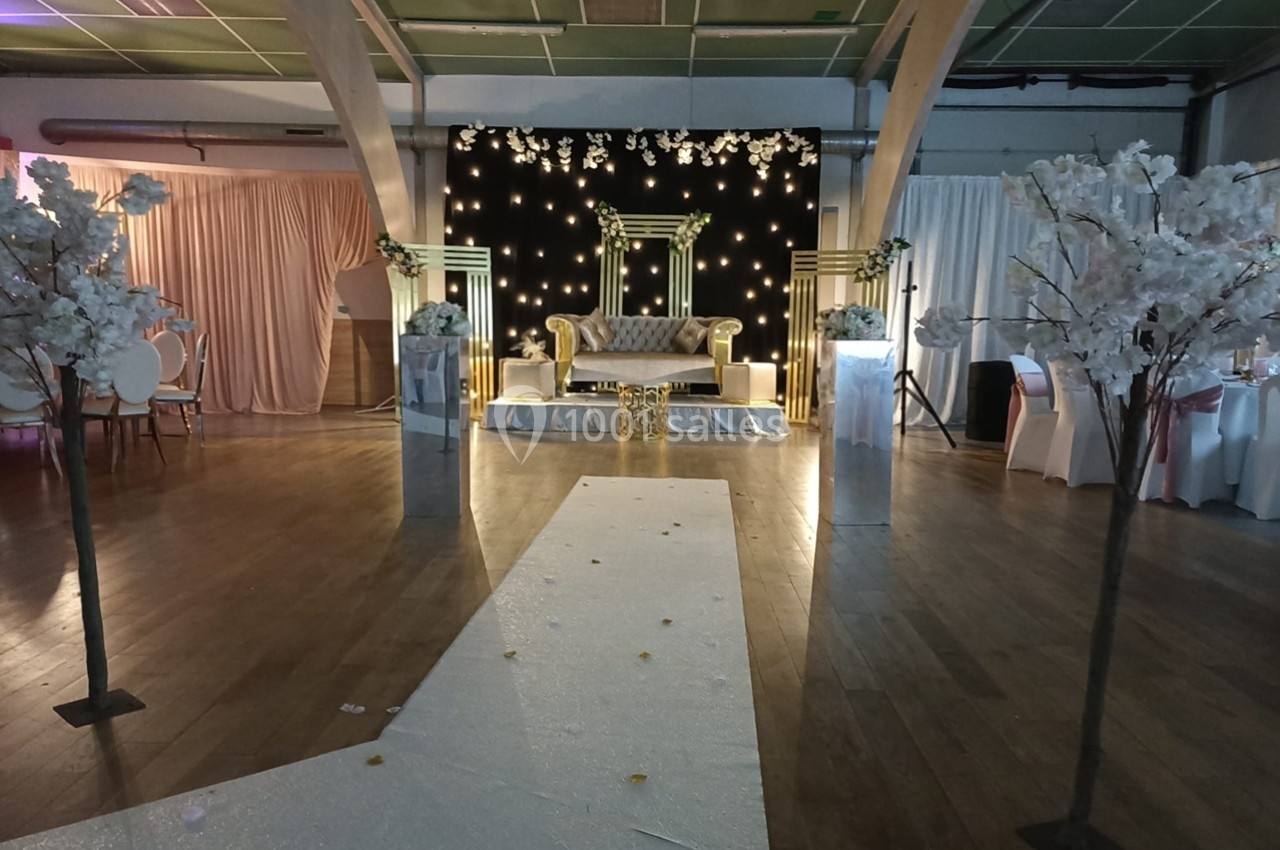 Décoration de salle de réception avec canapé doré sur scène, allée blanche et arbres artificiels fleuris.