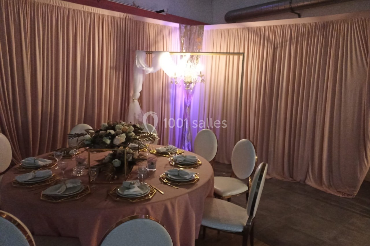 Table décorée pour un événement avec nappes roses, vaisselle élégante et centre de table floral, devant des rideaux roses.