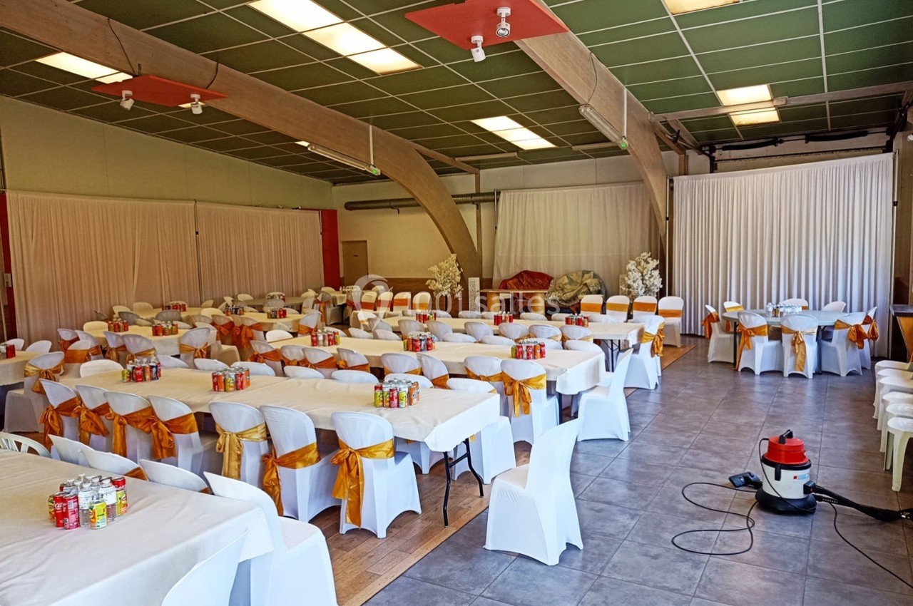 Salle de réception décorée avec des tables et chaises blanches ornées de nœuds orange, prête pour un événement.
