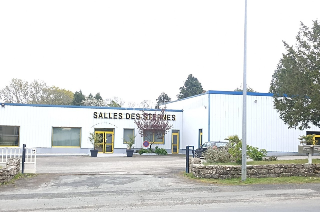 Bâtiment blanc avec enseigne ’Salles des Sternes’, entouré d'arbres et d'un parking à l'avant.