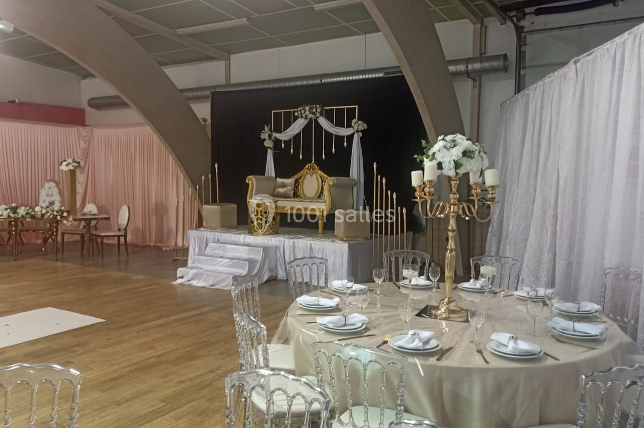 Salle de réception décorée avec des tables dressées, un canapé doré sur une estrade et des rideaux blancs en arrière-plan.