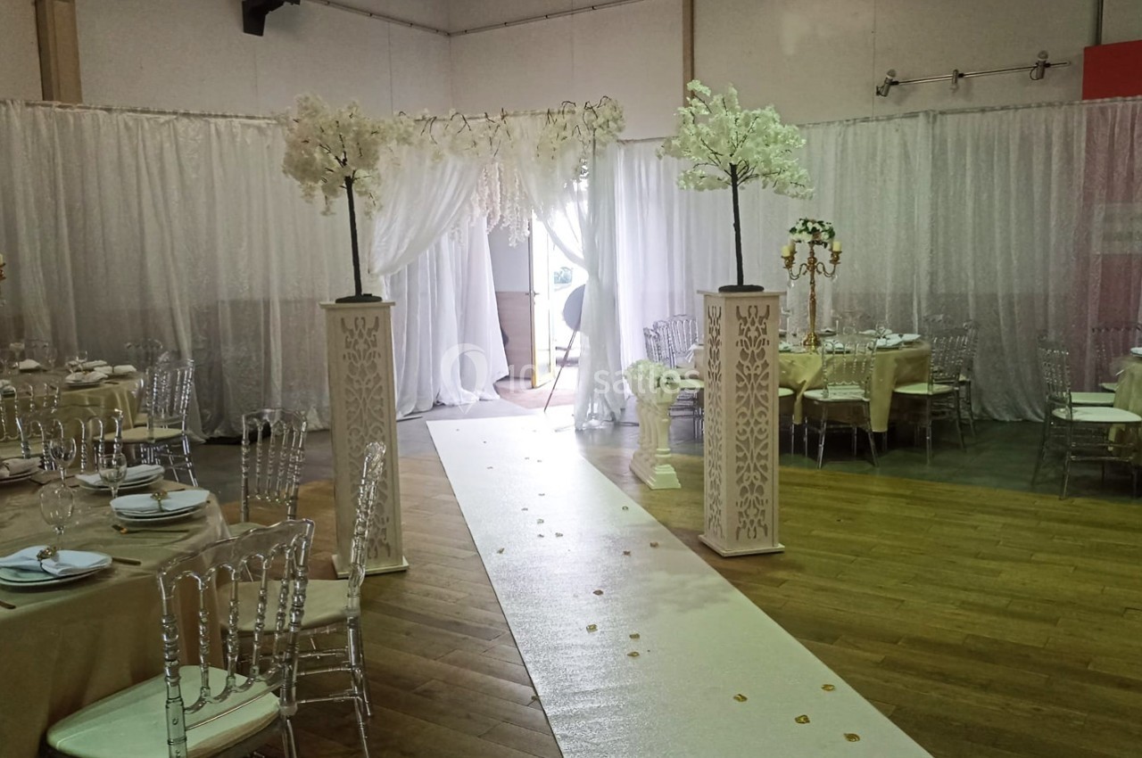 Salle de réception décorée avec des tables dressées, des chaises transparentes et une allée centrale ornée de colonnes et de…