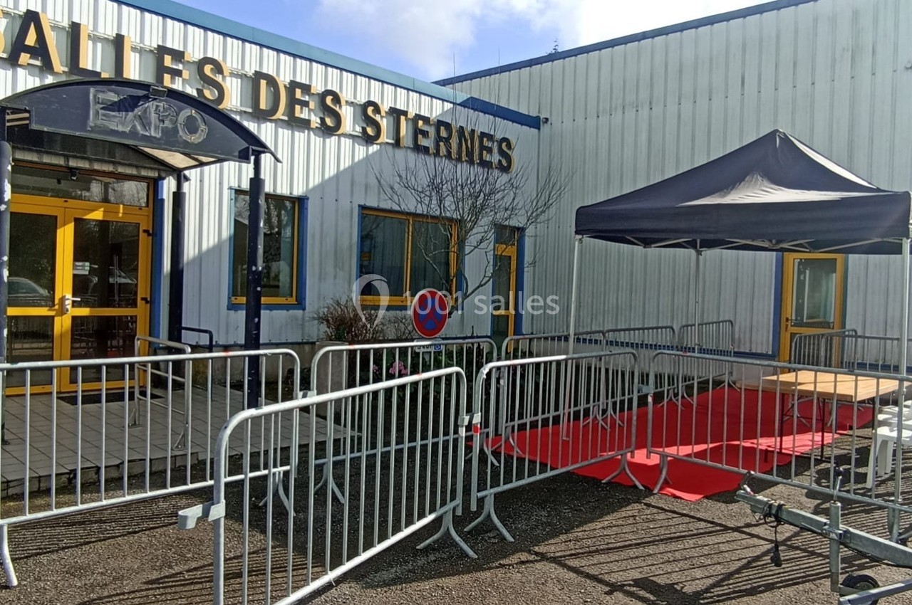 Entrée d'un bâtiment avec des barrières, un tapis rouge et une tente noire installés à l'extérieur.