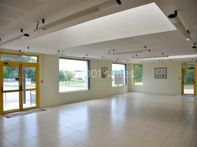 Salle lumineuse avec carrelage blanc, grandes fenêtres, murs clairs, et éclairage suspendu moderne.