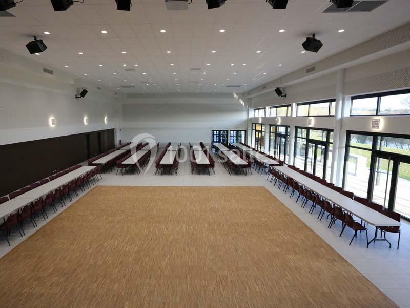 Salle spacieuse avec des tables et des chaises alignées, éclairée par de grandes baies vitrées.