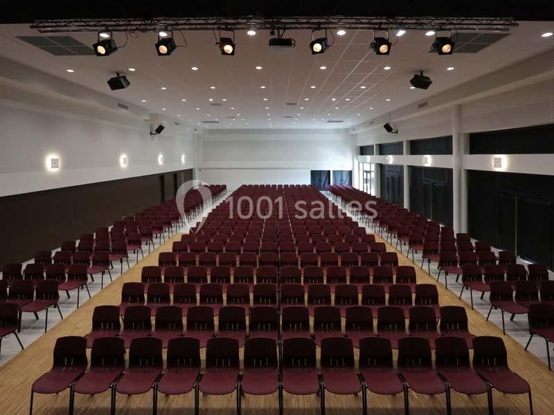 Salle de conférence vide avec des rangées de chaises rouges alignées et un éclairage au plafond.