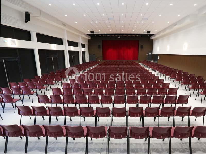 Salle de spectacle vide avec des rangées de chaises rouges alignées face à une scène avec un rideau rouge fermé.