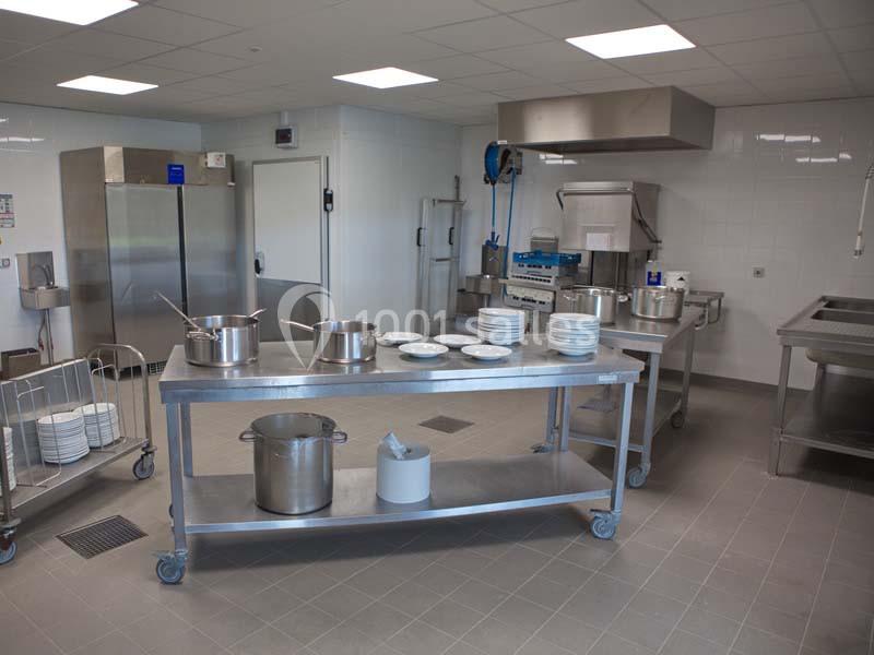 Cuisine professionnelle équipée avec plans de travail en inox, casseroles, assiettes empilées et appareils de cuisson.