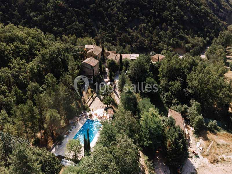 Vue aérienne d'un domaine entouré de forêt avec une piscine centrale et plusieurs bâtiments en pierre.