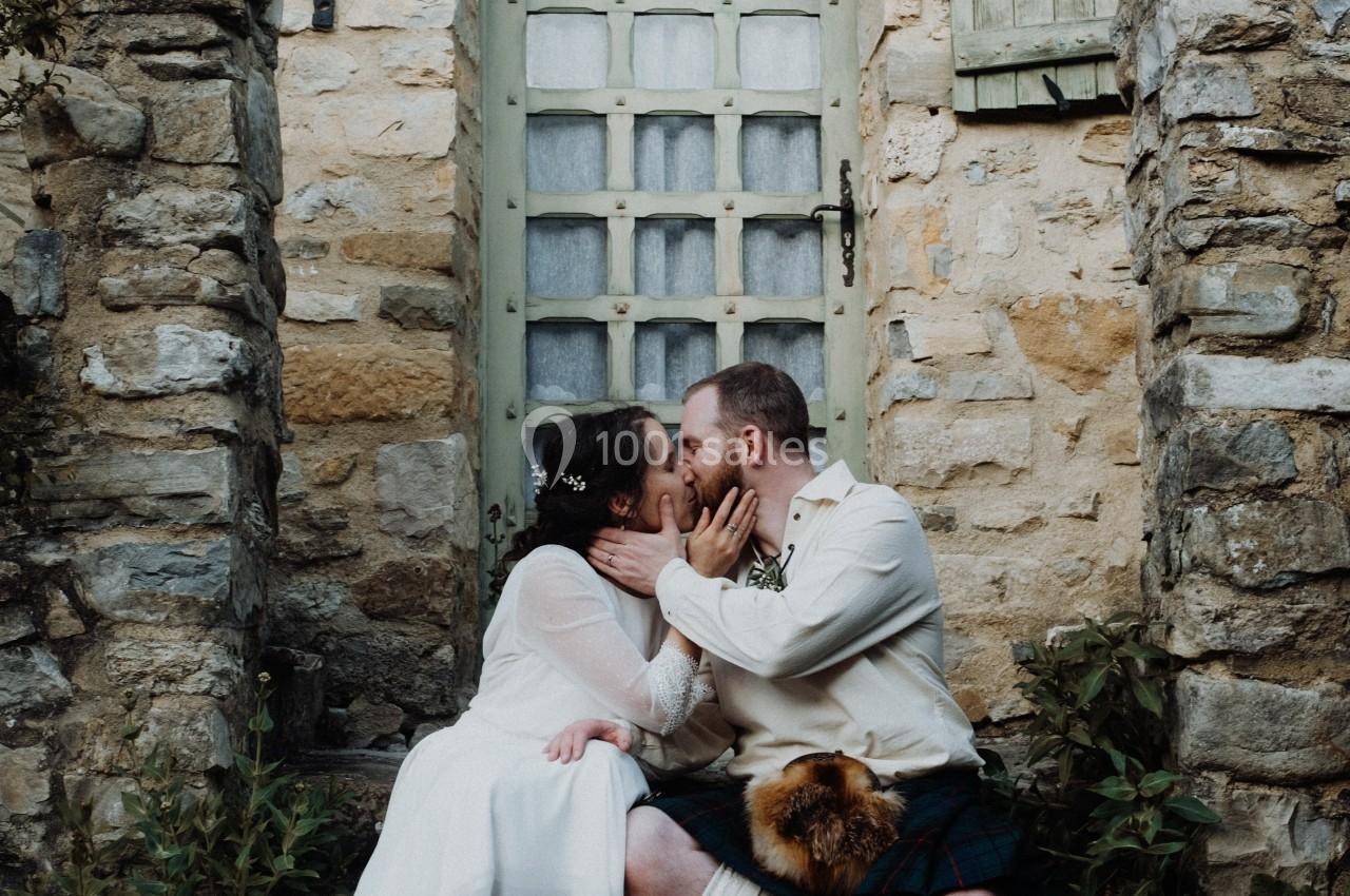 Un couple en tenue traditionnelle s'embrasse sur les marches d'une maison en pierre avec une porte vitrée.