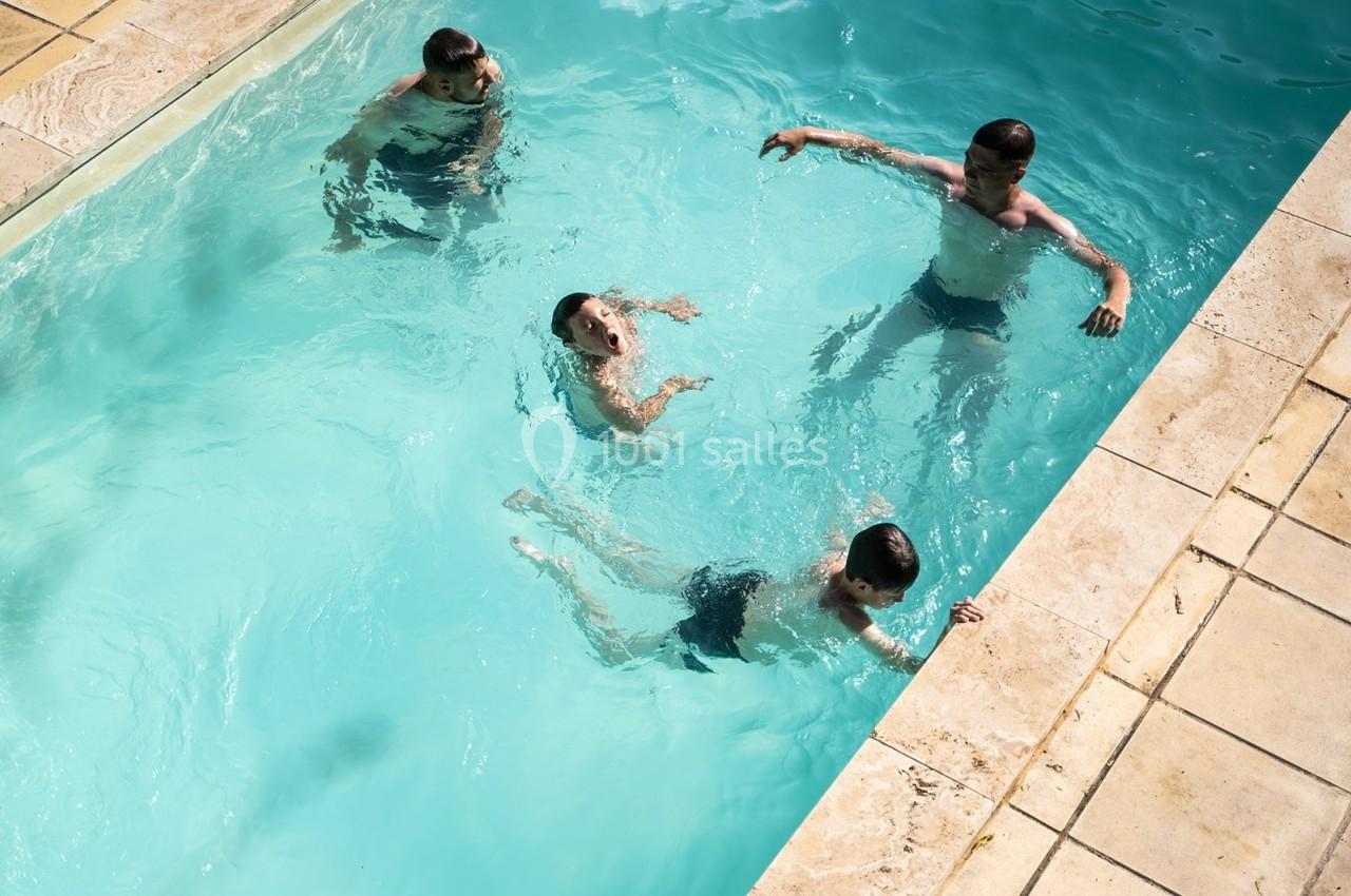 Quatre personnes nagent et jouent dans une piscine extérieure entourée de margelles en pierre.