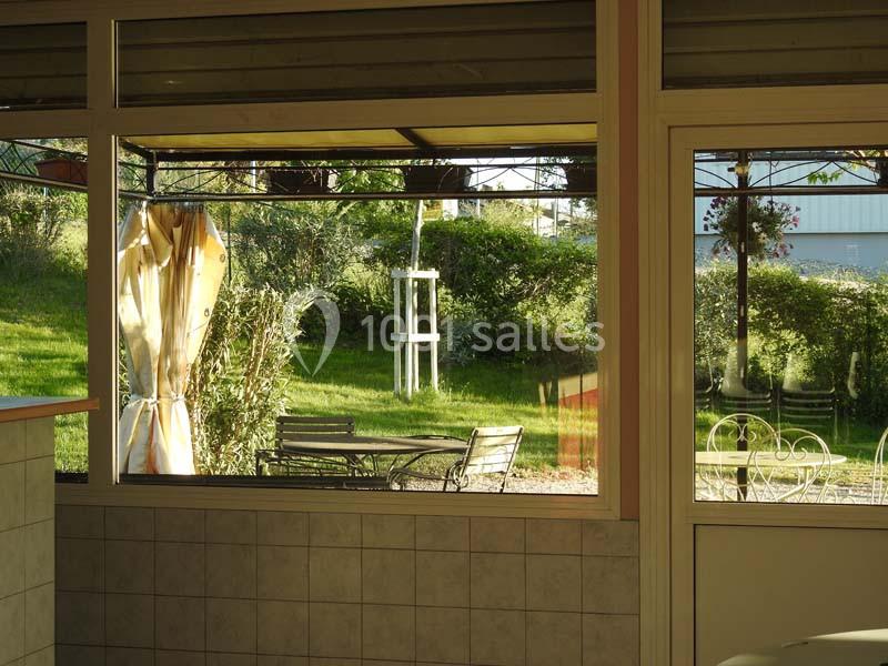 Vue depuis une fenêtre donnant sur un jardin avec des chaises, une table en métal et des arbres en arrière-plan.