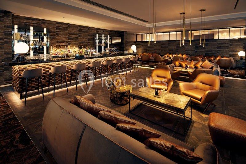 Location salle Nivelles (Brabant wallon) - Hôtel Nivelles Sud #19 Bar moderne avec comptoir en pierre, tabourets hauts, fauteuils en cuir et éclairage tamisé dans une ambiance chaleureuse.