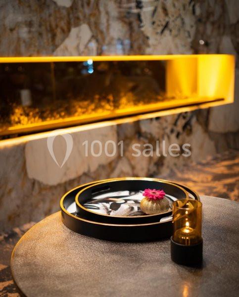 Location salle Nivelles (Brabant wallon) - Hôtel Nivelles Sud #18 Plateau décoratif avec une fleur rose et une bougie sur une table, devant un mur en marbre éclairé d'une lumière jaune.