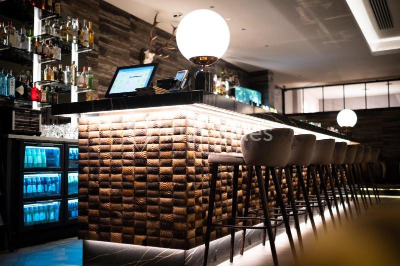 Location salle Nivelles (Brabant wallon) - Hôtel Nivelles Sud #20 Bar moderne avec comptoir éclairé, tabourets hauts, étagères de bouteilles et ambiance tamisée.