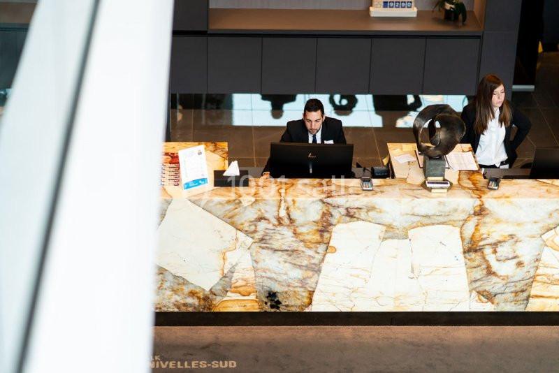 Location salle Nivelles (Brabant wallon) - Hôtel Nivelles Sud #9 Un réceptionniste et une employée travaillent derrière un comptoir en marbre dans un hall moderne.