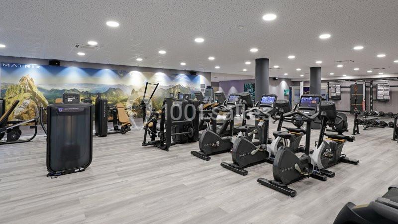 Location salle Nivelles (Brabant wallon) - Hôtel Nivelles Sud #23 Salle de sport moderne avec équipements de musculation, vélos d'exercice et décor mural représentant un paysage naturel.