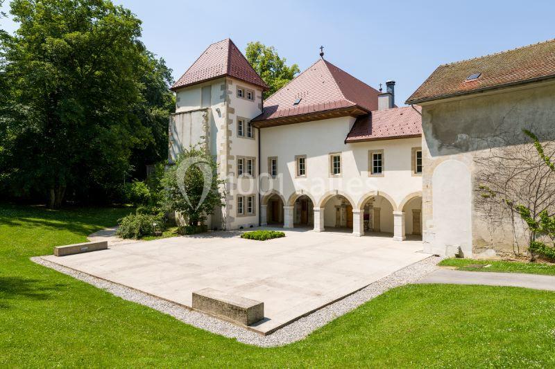 Façade d'un bâtiment historique avec une cour pavée, entouré de pelouses et d'arbres.