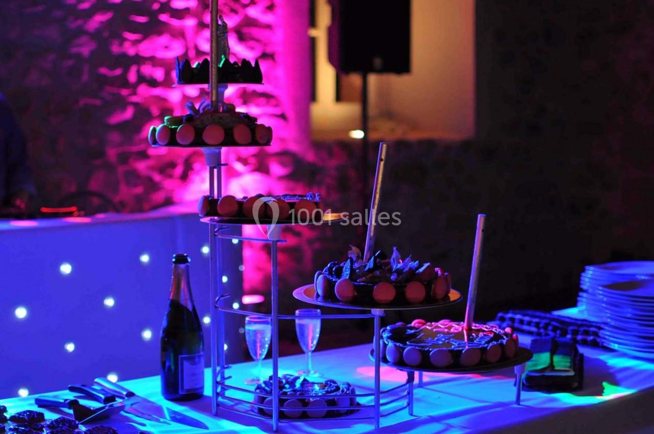 Plateau de desserts éclairé par des lumières colorées, avec une bouteille de champagne et des verres sur la table.