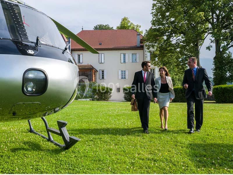 Un hélicoptère posé sur une pelouse près d'un bâtiment, trois personnes en tenue professionnelle marchent à proximité.