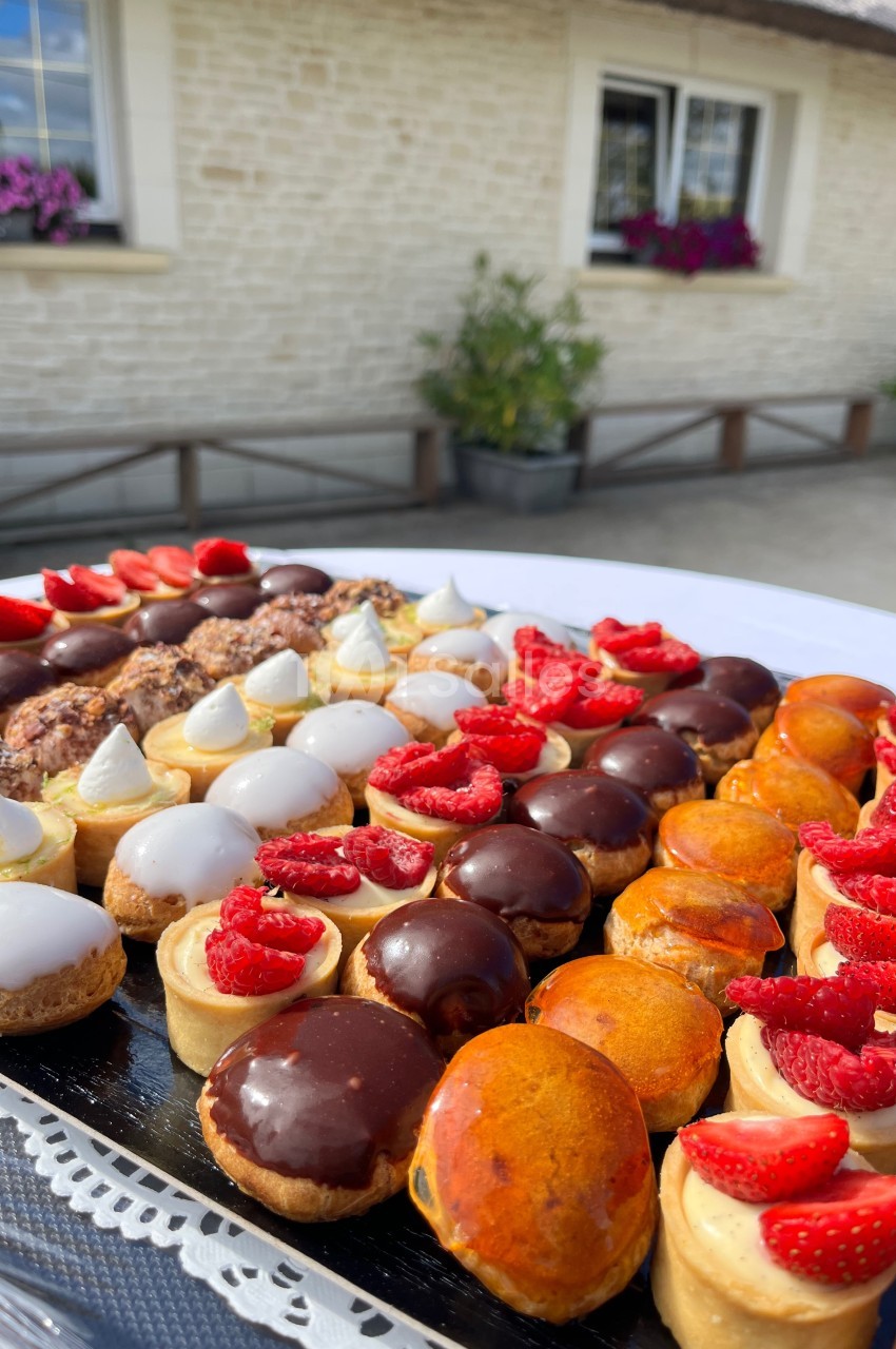 Plateau de pâtisseries variées avec glaçages brillants et décorations de fraises, posé sur une table en extérieur.