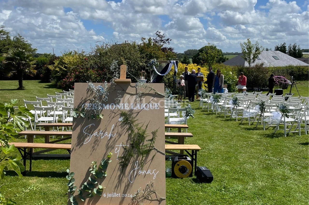 Panneau annonçant une cérémonie laïque dans un jardin avec des chaises blanches disposées pour les invités.
