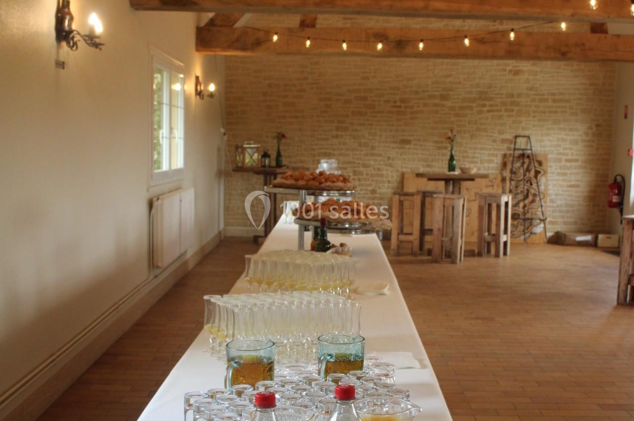 Table dressée avec boissons, verres et viennoiseries dans une salle lumineuse aux murs en pierre et poutres apparentes.