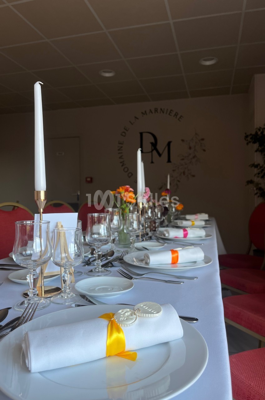 Table dressée élégamment avec vaisselle blanche, bougies, verres et décorations florales colorées dans une salle sobre.