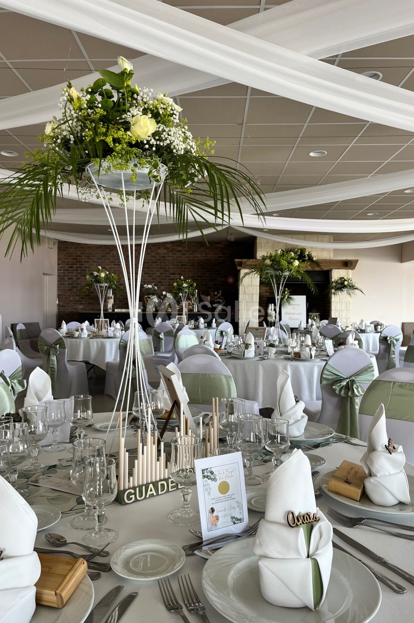 Salle de réception décorée pour un mariage, avec tables dressées, nappes blanches et centres de table fleuris.