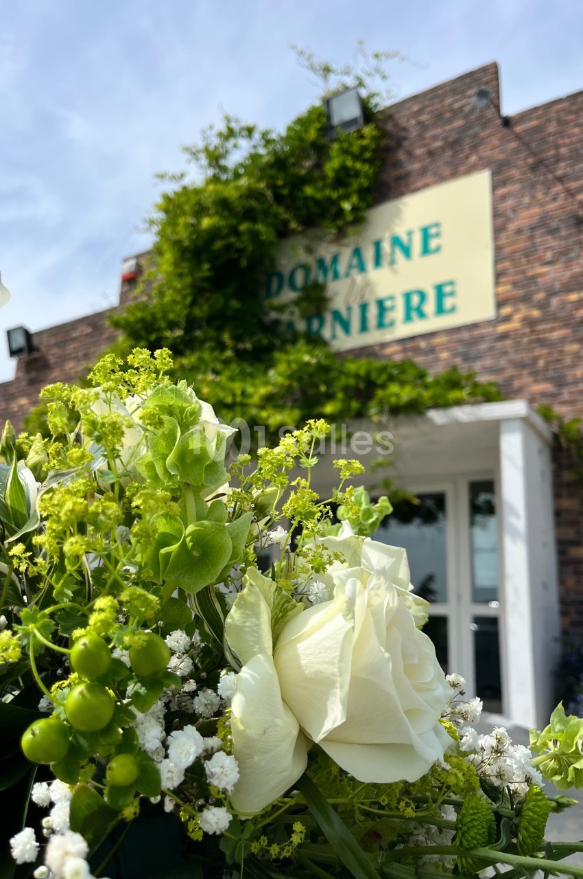 Bouquet de fleurs blanches et vertes au premier plan devant un bâtiment en briques avec une enseigne ’Domaine Garnier’.