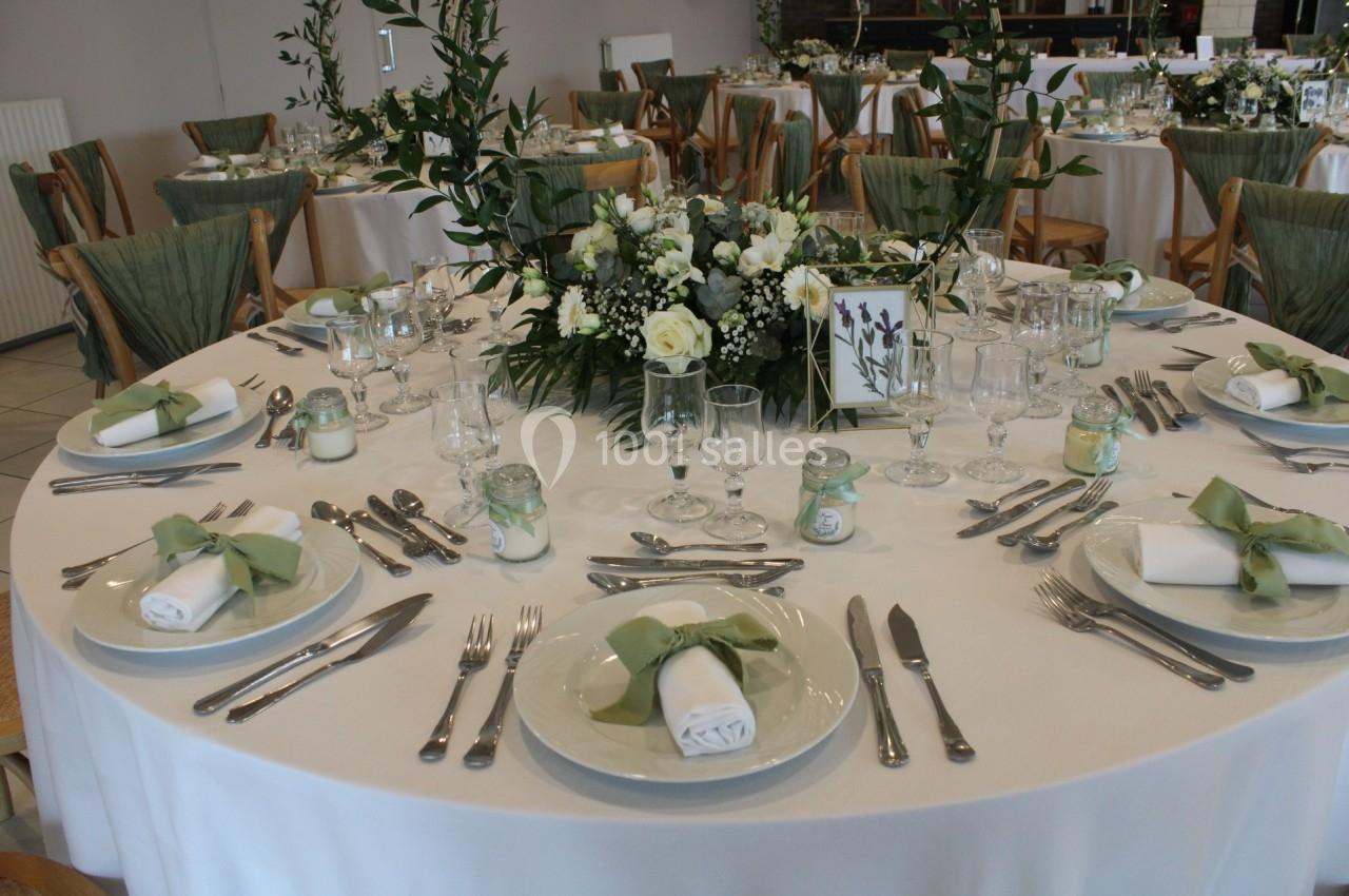 Table ronde élégamment dressée avec nappes blanches, serviettes nouées, vaisselle raffinée et centre de table floral.