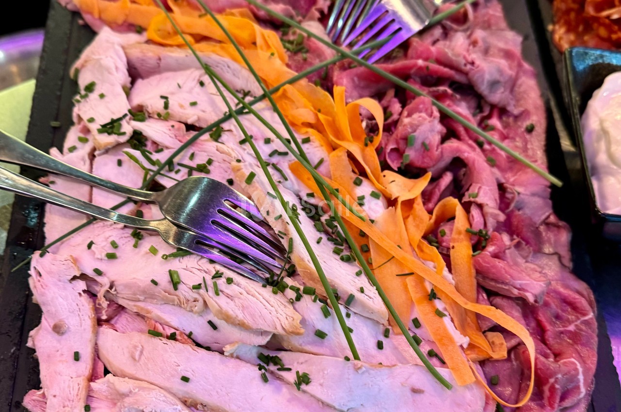 Plateau de tranches de viande blanche et rouge garnies de ciboulette et de lamelles de carotte, avec des fourchettes.