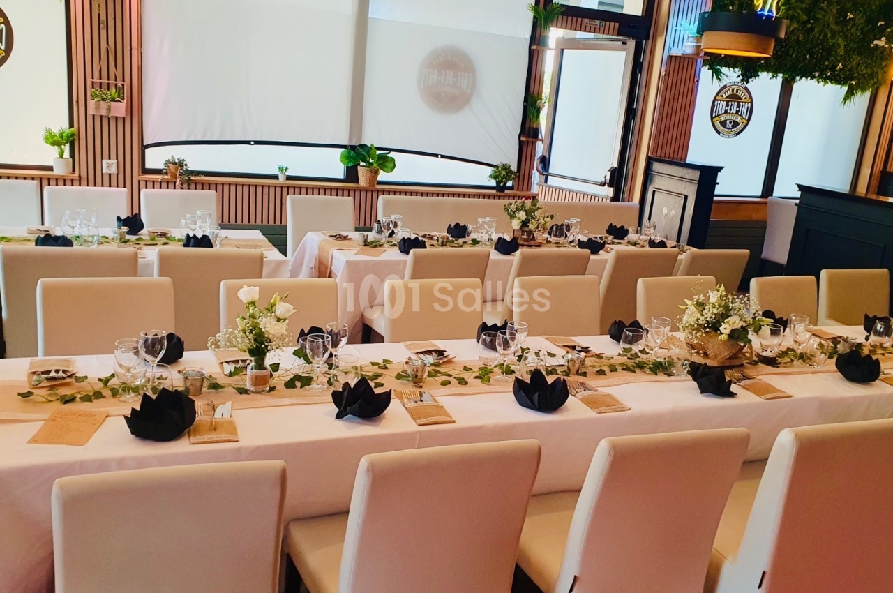 Salle de réception décorée avec des tables dressées, nappes blanches, serviettes noires pliées et arrangements floraux.