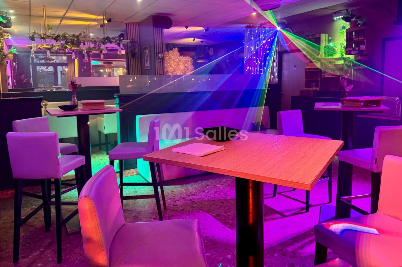Salle de bar avec tables hautes, chaises, éclairage coloré et effets lumineux dans une ambiance festive.