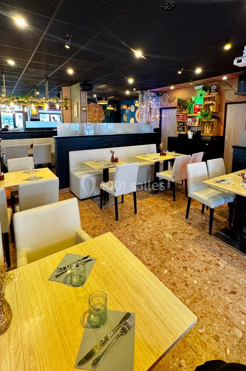 Salle de restaurant lumineuse avec tables en bois clair, chaises rembourrées et décoration végétale suspendue.