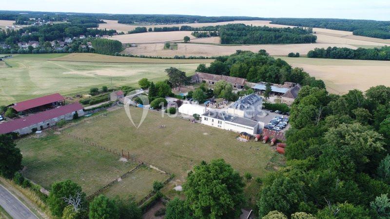 Vue aérienne d'un domaine rural avec bâtiments, champs cultivés, forêt et routes environnantes.