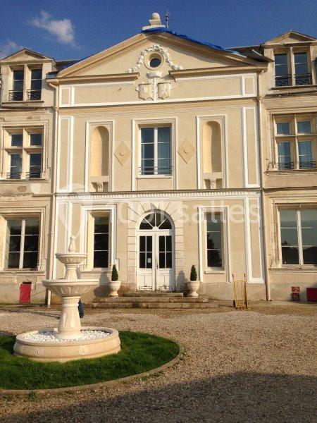 Façade d'un bâtiment ancien beige avec des fenêtres symétriques, une fontaine blanche au premier plan.
