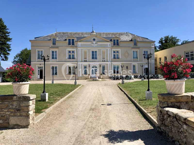 Façade d'un grand bâtiment de style classique entouré de pelouses, avec des pots de fleurs et une allée centrale.