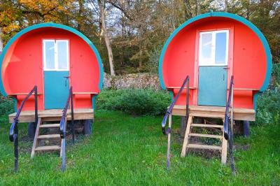 Deux roulottes rouges avec portes vertes, posées sur un terrain herbeux devant des arbres en automne.