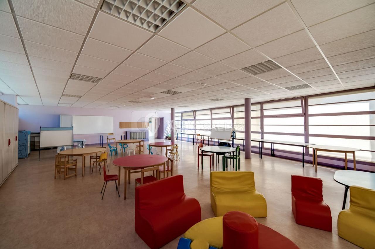 Salle lumineuse avec des tables, chaises et fauteuils colorés, aménagée pour des activités éducatives ou récréatives.