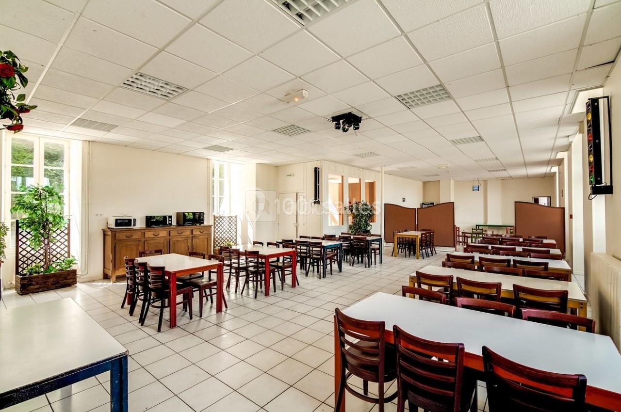 Salle de restauration lumineuse avec tables et chaises en bois, carrelage blanc et grandes fenêtres.